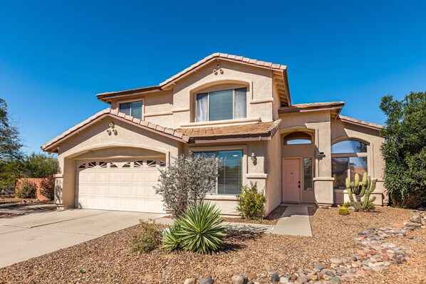 A two-story house with a garage, a small tree, and a cactus garden.