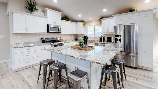 A modern kitchen with white cabinets, stainless steel appliances, and a central island with stools. - Modern Ranch with Private Putting Green, Fast WiFi, Central AC, & Great Location (Scottsdale)
