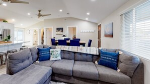 A modern living room with a grey sectional sofa, ceiling fans, recessed lighting, and a dining area with blue chairs. - Modern Ranch with Private Putting Green, Fast WiFi, Central AC, & Great Location (Scottsdale)