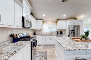 A modern kitchen with white cabinets, granite countertops, stainless steel appliances, and a central island. - Modern Ranch with Private Putting Green, Fast WiFi, Central AC, & Great Location (Scottsdale)