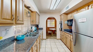 A kitchen with wooden cabinets, a granite countertop, a stainless steel refrigerator, and a dining area with a table and chairs. - Fun, Dog-Friendly Home w/ Game Room, Ping-Pong, Patio, Fast WiFi, & AC (Tucson)