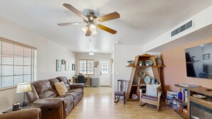 A spacious living room with a ceiling fan, a wooden floor, a sofa, a chair, and a TV stand. - Fun, Dog-Friendly Home w/ Game Room, Ping-Pong, Patio, Fast WiFi, & AC (Tucson)