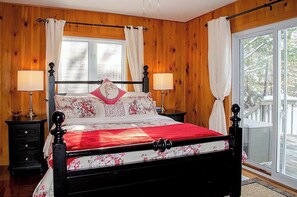 A wooden-paneled bedroom with a bed, two bedside tables, and a window with curtains.
