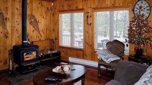 A cozy cabin interior with a wood-burning stove, a Christmas tree, and large windows. - Mapleview - Three Bedroom Cottage, Sleeps 12 (Cloyne)