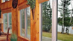 A wooden interior with large windows, a clock, and a plant. - Mapleview - Three Bedroom Cottage, Sleeps 12 (Cloyne)