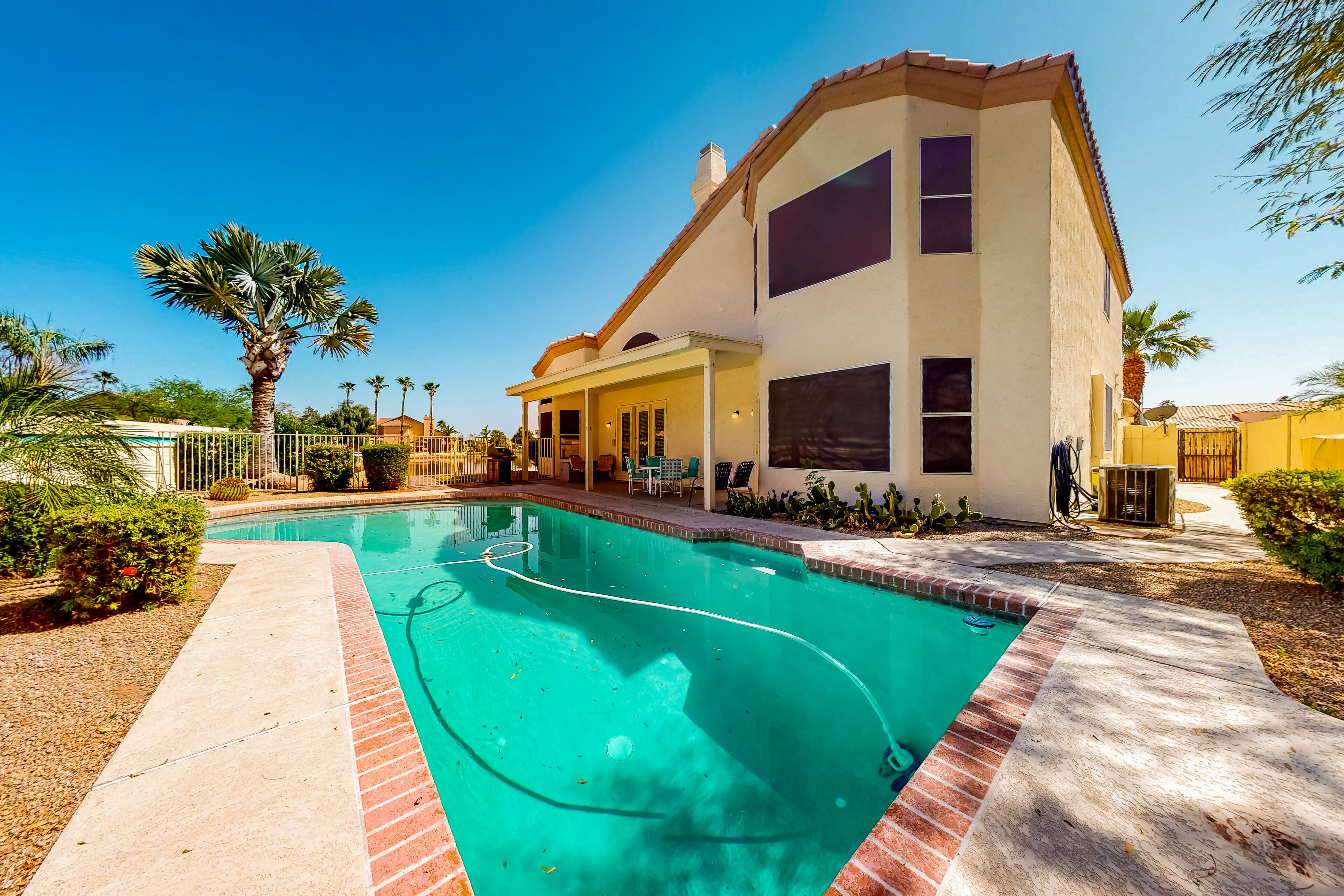 Una casa moderna de dos pisos con piscina, rodeada de palmeras y un jardín bien cuidado.