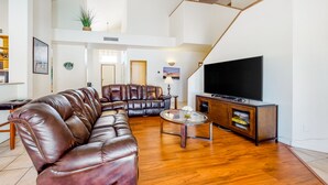 Een ruime woonkamer met een bruine leren bank, een glazen salontafel en een flatscreen televisie op een houten kast.