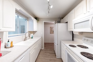 A modern kitchen with white appliances, a window with blinds, and a wooden floor. - Dog-Friendly Home near Downtown with Private Patio, Gas Grill, Central A/C, W/D (Sun City)