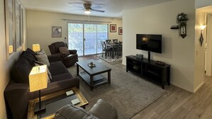 A living room with a sofa, coffee table, TV, and a dining area with chairs and a table. - Dog-Friendly Home near Downtown with Private Patio, Gas Grill, Central A/C, W/D (Sun City)