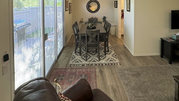 A living room with a brown leather sofa, a dining area with a glass table and chairs, and a patterned rug on the floor. - Dog-Friendly Home near Downtown with Private Patio, Gas Grill, Central A/C, W/D (Sun City)