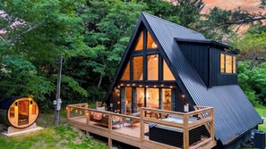 Ein modernes A-Haus mit einer Terrasse, großen Fenstern und einem kleinen Anbau.