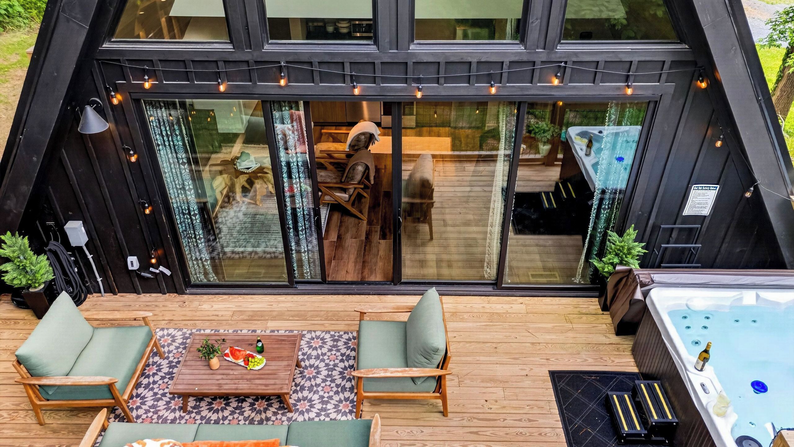 A modern, compact living space with a large sliding glass door, a wooden deck, outdoor seating, and a hot tub.