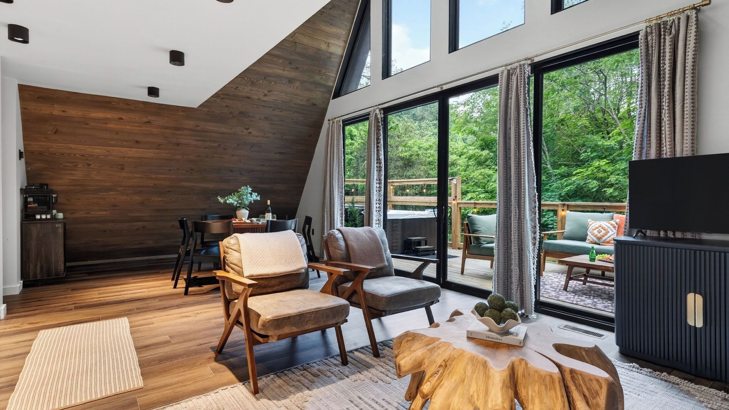 Un salon moderne avec un plafond en bois, de grandes fenêtres et une vue sur la verdure.