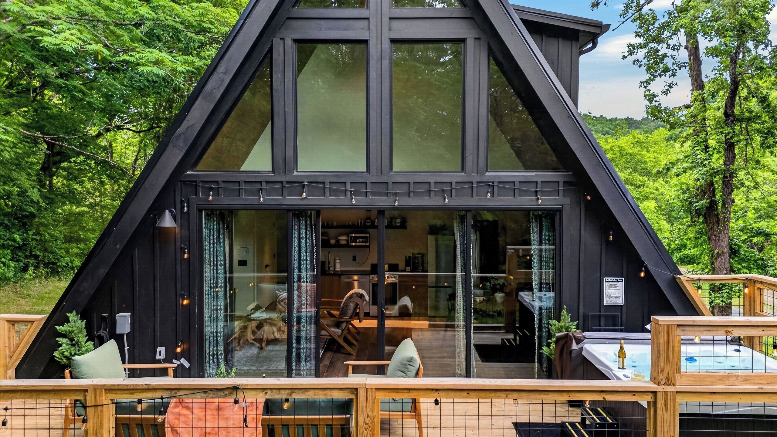 Ein modernes A-Haus mit großen Fenstern, einer Holzterrasse und einem Whirlpool.