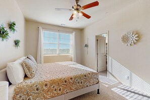 Ein Schlafzimmer mit Bett, Deckenventilator, Fenster mit Jalousien und einer Tür.