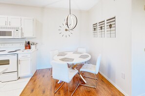 A modern kitchen with white cabinetry, a microwave, and a dining area with a round table and white chairs.