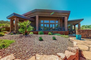 A modern house with a covered patio, a stone foundation, and a landscaped garden. - Custom luxury home with Cathedral Rock views, outdoor living, hot tub, & firepit (Sedona)