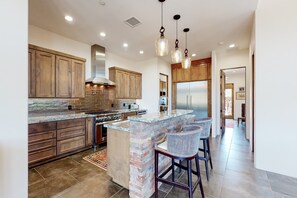 A modern kitchen with wooden cabinets, a central island, and bar stools. - Custom luxury home with Cathedral Rock views, outdoor living, hot tub, & firepit (Sedona)