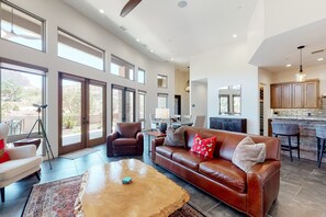 A spacious living area with a leather sofa, a coffee table, and a dining area with bar stools. - Custom luxury home with Cathedral Rock views, outdoor living, hot tub, & firepit (Sedona)