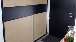 Um quarto com porta deslizante, porta preta, luminária pendente cinza, uma pequena mesa com um vaso vermelho e um tapete preto no chão.