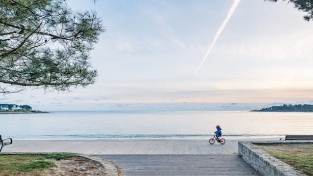 Um calçadão de madeira que dá para uma praia, com uma pessoa andando de bicicleta.
