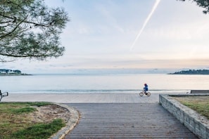 En träpromenad som leder till en strand, och på den cyklar en person.