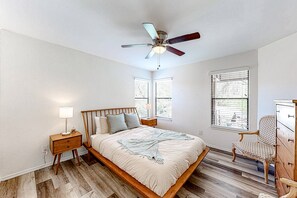 Een slaapkamer met een houten bed, een nachtkastje met een lamp, een stoel, een dressoir en een plafondventilator.