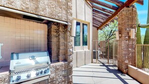 An outdoor barbecue grill attached to a stone wall, a covered patio area, and a cactus in the background.
