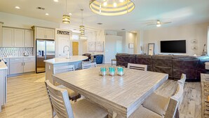 Una cocina moderna con una isla central, un comedor con sillas, una sala de estar con sofá y televisor.