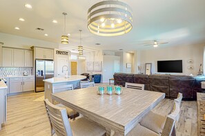 A modern kitchen with a central island, a dining area with chairs, a living room with a sofa, and a TV. - Snowbird-friendly home with WiFi, central AC, enclosed yard, pool, and patio (Tucson)