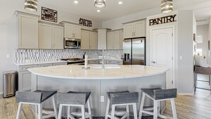 Una cocina moderna con una isla central, taburetes de bar y un letrero que dice 'PANTRY'.