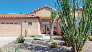 Una casa residencial con garaje, puerta principal y un pequeño jardín con un cactus y una palmera.