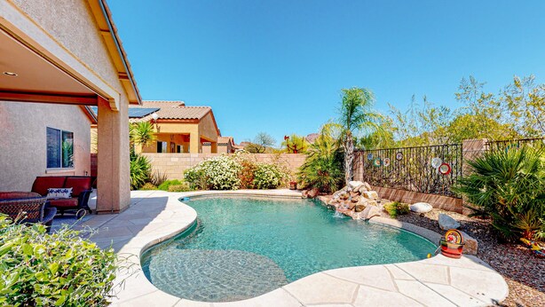 Una piscina de diseño curvo, rodeada por una terraza con mobiliario exterior y una pequeña cascada.