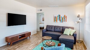 Ein modernes Wohnzimmer mit Fernseher, grauem Sofa, einer Holzunterhaltungsecke und einem gemusterten Teppich.