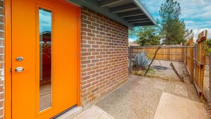 Ein Ziegelhaus mit einer orangenen Tür und einer überdachten Terrasse.