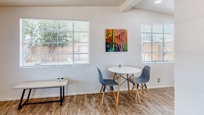 Ein Zimmer mit einem weißen Tisch, zwei Stühlen, einer Bank und einem farbenfrohen Gemälde an der Wand.
