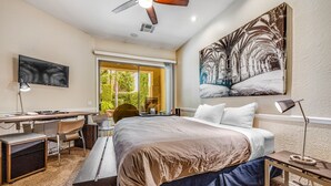 Una camera da letto con un grande letto, una scrivania, una sedia, una TV e una ventola a soffitto.