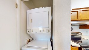 Eine kompakte Küche mit weißem Wäschewascher und Trockner, Holzschränken und einem Edelstahlbackofen.