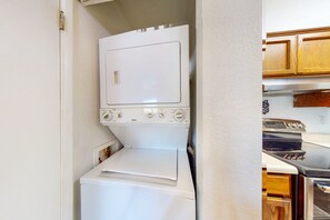 Eine kompakte Küche mit weißem Wäschewascher und Trockner, Holzschränken und einem Edelstahlbackofen.