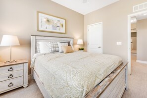 Ein Schlafzimmer mit Bett, Nachttischen, einer Tür und einem gerahmten Bild an der Wand.