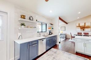 A modern kitchen with blue cabinets, white countertops, and a built-in dishwasher. There is a dining area with a table and chairs, and a large abstract painting on the wall. - Sunny South Tempe gem with enclosed yard, covered lanai, grill, & washer/dryer (Tempe)