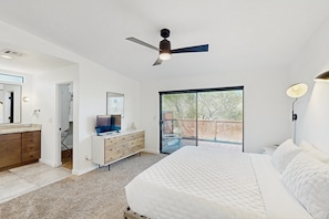 A bedroom with a bed, a ceiling fan, a TV, a dresser, a large window, and a sliding glass door leading to an outdoor area. - Gorgeous private home w/ private pool & hot tub, large yard & amazing views (Tucson)