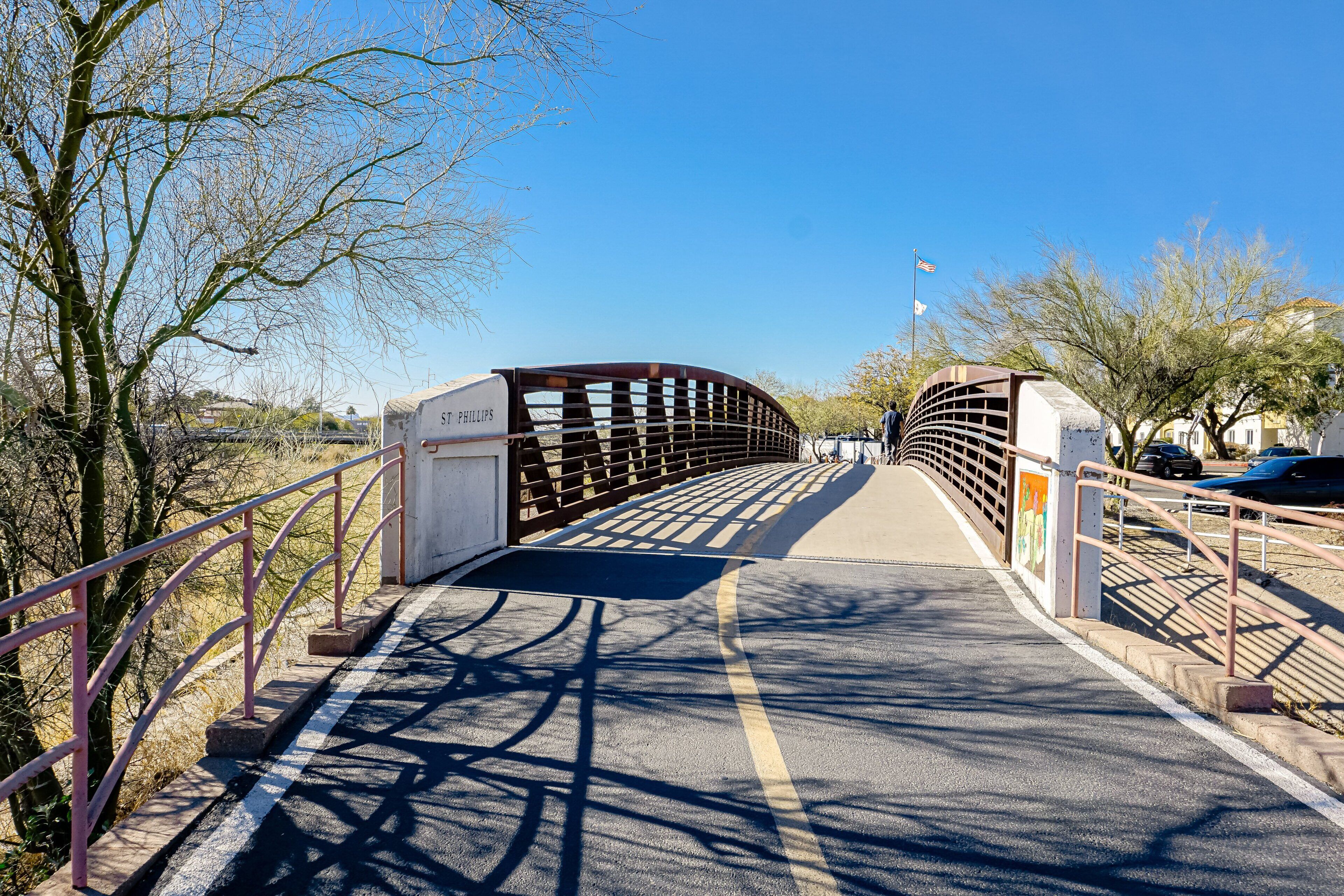 Un pont piétonnier avec une rambarde en métal, un ciel dégagé et des arbres de chaque côté.