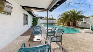 Zona de piscina con un porche cubierto, mobiliario exterior y una canasta de baloncesto.
