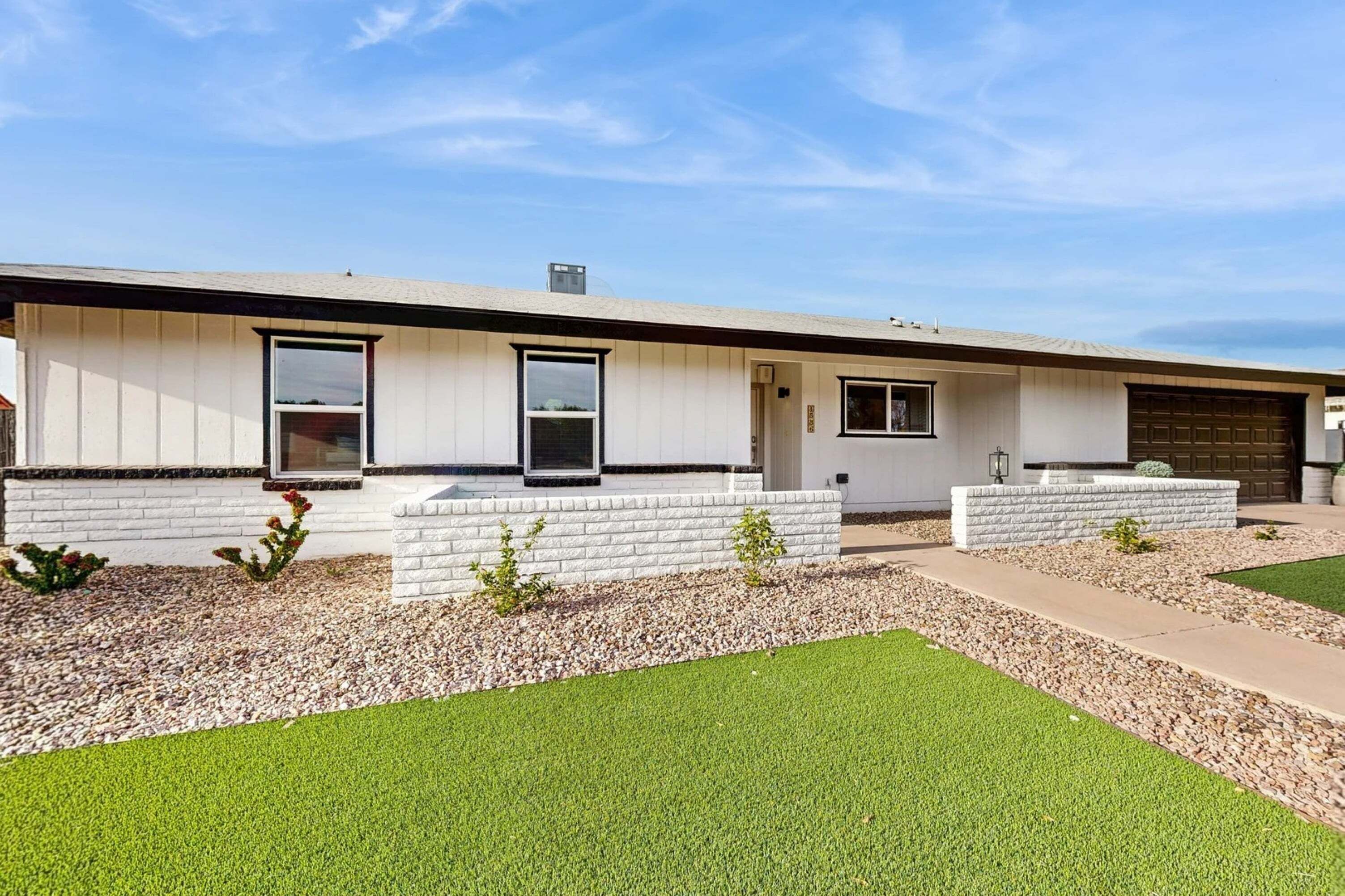 Une maison moderne de plain-pied, dotée d’un toit plat, de murs extérieurs blancs et d’un garage à l’avant.
