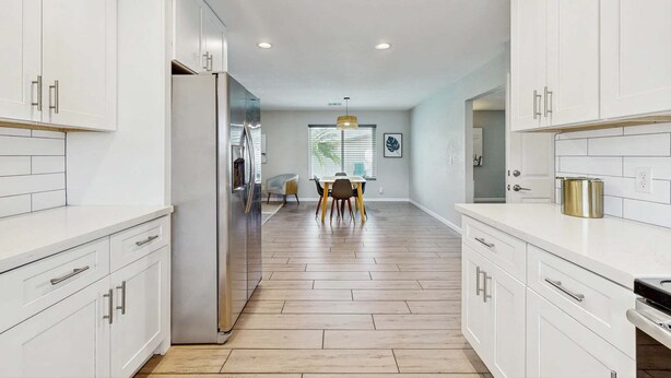 Una cocina moderna con armarios blancos, un refrigerador de acero inoxidable y una zona de comedor con mesa y sillas.