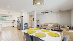 Una cocina moderna con armarios blancos, un refrigerador de acero inoxidable y un comedor con una mesa y sillas blancas.