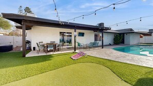 Un patio techado con mobiliario exterior, una piscina y luces colgantes.
