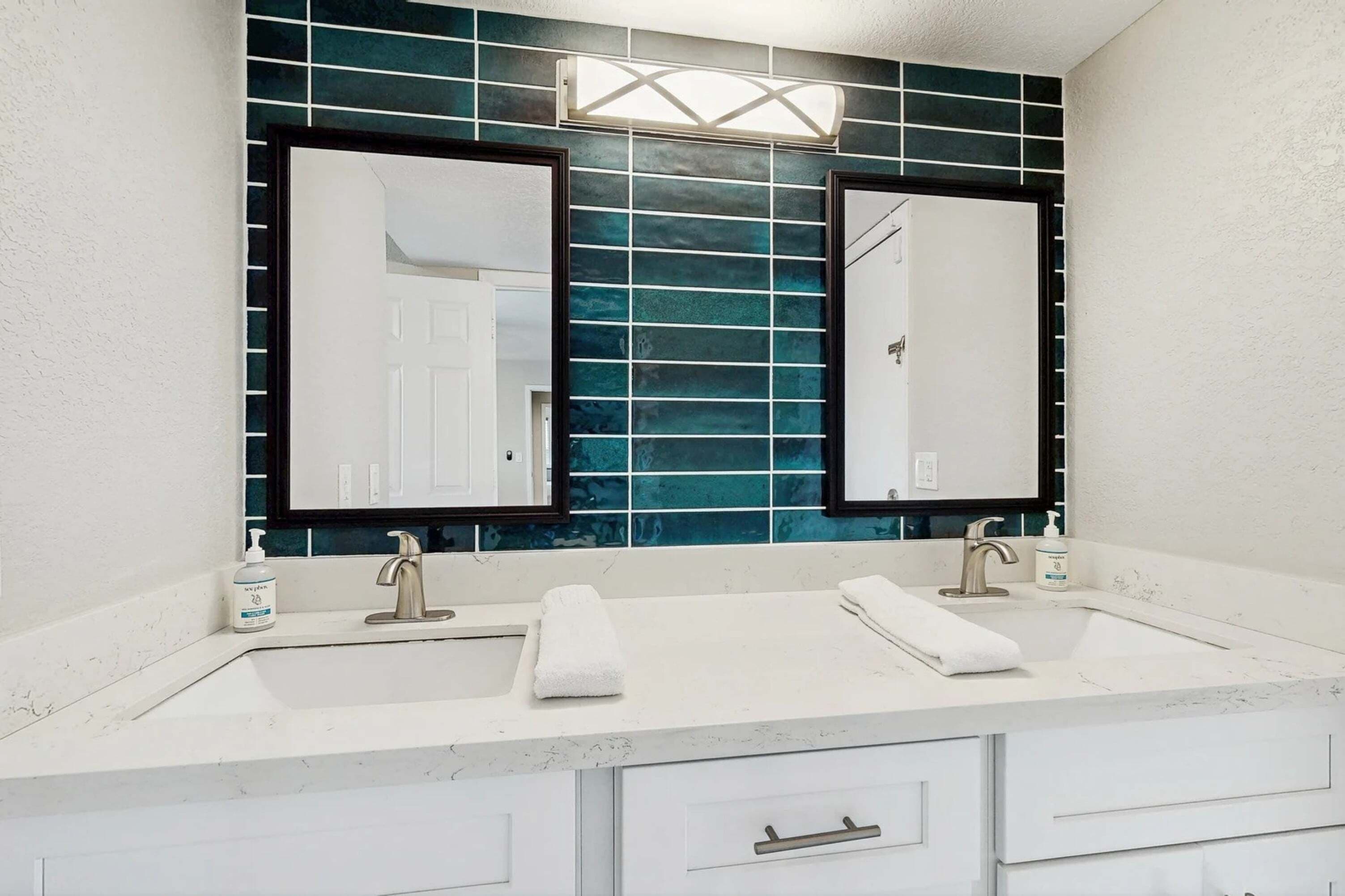 A bathroom with two sinks, a mirror, and a wall with blue tiles.