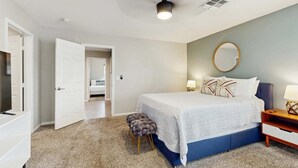 Un dormitorio con cama, un espejo redondo, una mesita de noche y una puerta que da a otra habitación.